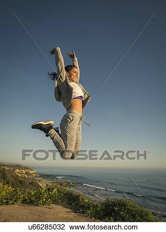 Stock Image - USA, California, Newport Beach, Woman jumping against clear sky. Fotosearch
