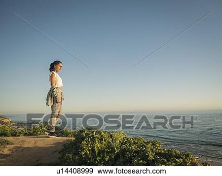 Stock Photo - USA, California, Newport Beach, Woman standing on cliff and looking at view. Fotosearch