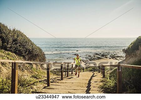 Stock Photo - USA, California, Newport Beach, Woman running up stairs. Fotosearch