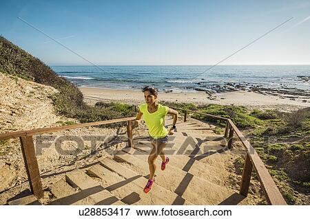Stock Photo - USA, California, Newport Beach, Woman running up stairs. Fotosearch