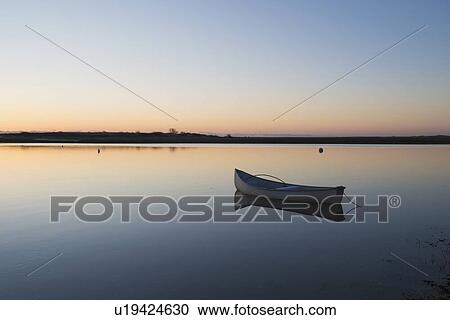 Stock Image - USA, Massachusetts, Cape Cod, Chatham, Boat reflecting in water at dawn. Fotosearch