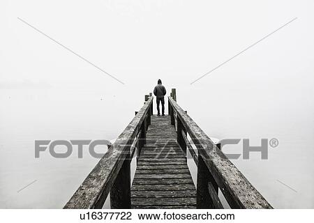 Stock Image - USA, Massachusetts, Cape Cod, Eastham, Man standing on jetty in fog. Fotosearch