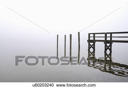 Stock Image - USA, Massachusetts, Cape Cod, Eastham, Wooden posts and jetty in fog. Fotosearch
