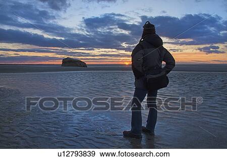 Stock Photo - USA, Massachusetts, Cape Cod, Orleans, Man watching sunset at beach. Fotosearch