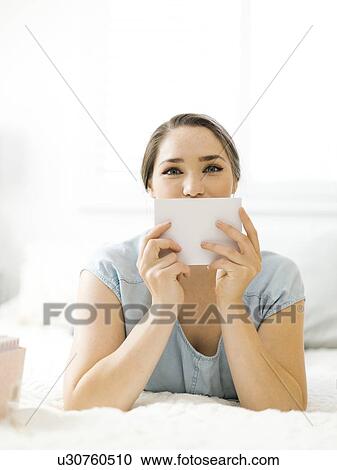 Stock Image - Woman holding envelope on bed. Fotosearch
