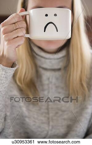 Woman holding mug with sad face in front of face View Large Photo Image Stock Image - Woman holding mug with sad face in front of face. Fotosearch