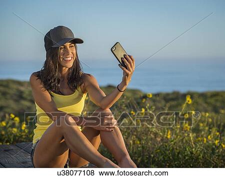 Stock Photo - Woman in baseball cap taking selfie. Fotosearch