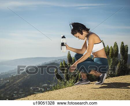 Woman in sportswear crouching with water bottle View Large Photo Image Stock Photo - Woman in sportswear crouching with water bottle. Fotosearch
