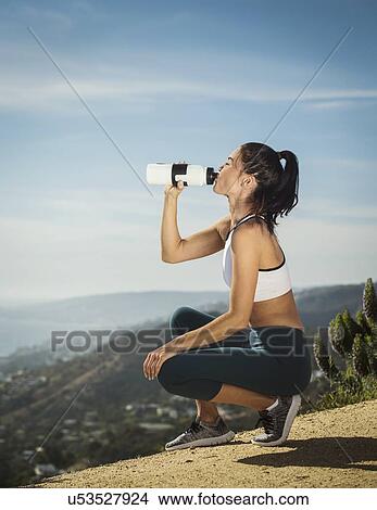 Picture - Woman in sportswear drinking water from bottle. Fotosearch