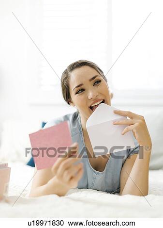 Stock Image - Woman licking envelope on bed. Fotosearch