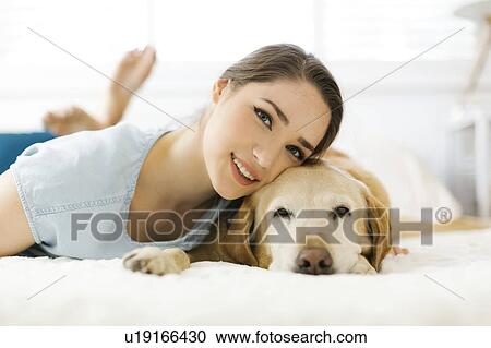 Stock Image - Woman lying on bed with dog. Fotosearch