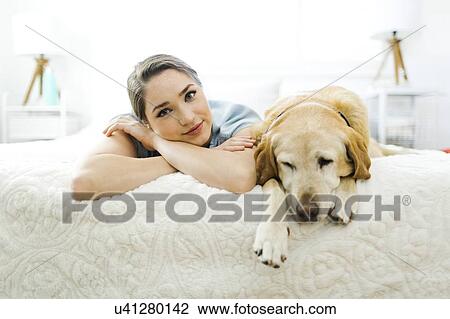 Stock Image - Woman lying on bed with dog. Fotosearch