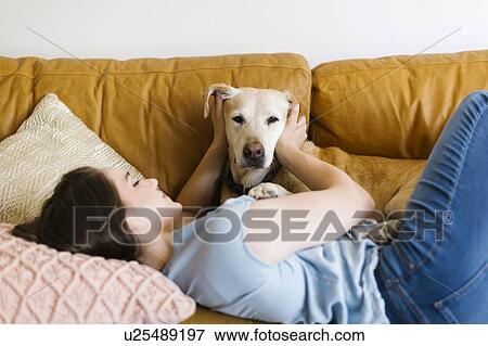 Stock Photo - Woman lying on sofa with dog. Fotosearch