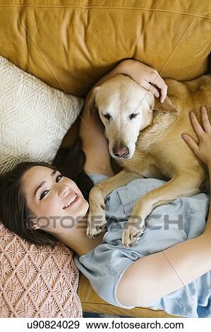 Stock Photo - Woman lying on sofa with dog. Fotosearch