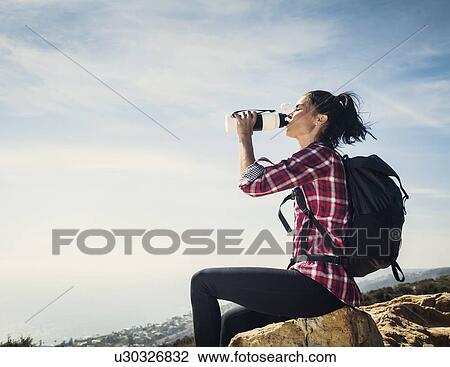 Woman on hike drinking water while sitting on rock View Large Photo Image Stock Image - Woman on hike drinking water while sitting on rock. Fotosearch
