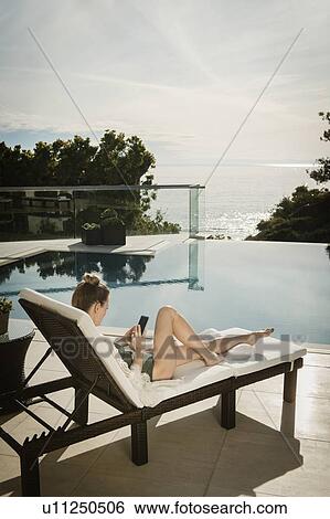 Stock Photograph - Woman relaxing by swimming pool. Fotosearch