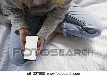 Stock Photo - Woman sitting in bed with smartphone. Fotosearch