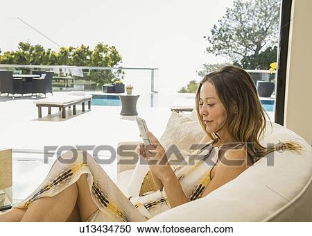 Stock Image - Woman sitting on sofa using smart phone. Fotosearch