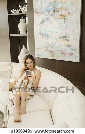 Stock Photography - Woman sitting on sofa using smart phone. Fotosearch