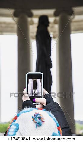Stock Image - Woman taking photograph of statue with smart phone. Fotosearch
