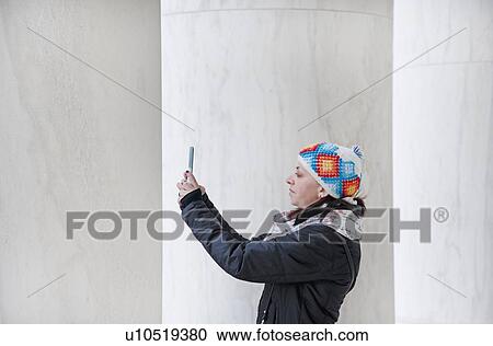 Stock Image - Woman taking photograph with smart phone by pillars. Fotosearch