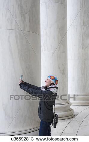 Stock Image - Woman taking selfie by pillars. Fotosearch
