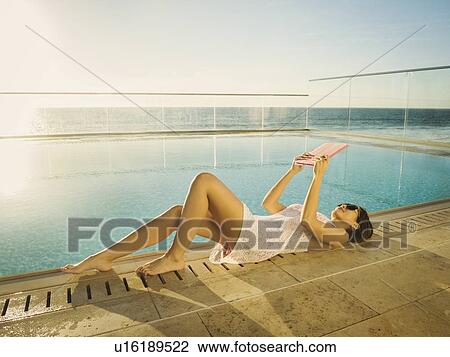 Stock Image - Woman using digital tablet by swimming pool. Fotosearch