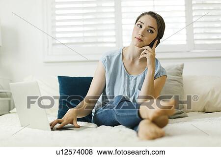 Stock Photo - Woman using laptop and smart phone on bed. Fotosearch