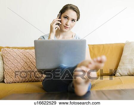 Stock Photo - Woman using laptop and smart phone on sofa. Fotosearch