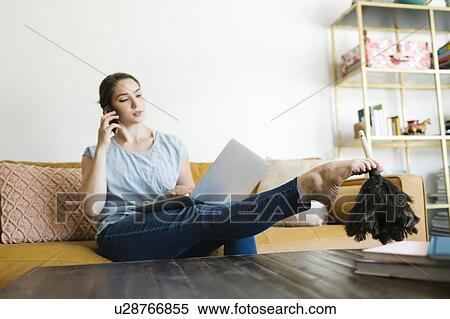 Stock Photography - Woman using laptop and smart phone while dusting with foot. Fotosearch