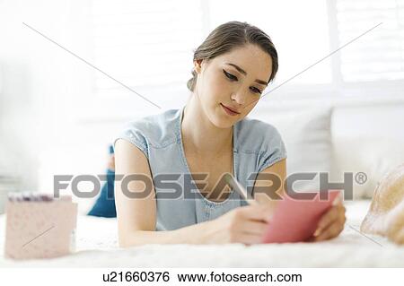 Stock Photograph - Woman writing in card on bed. Fotosearch