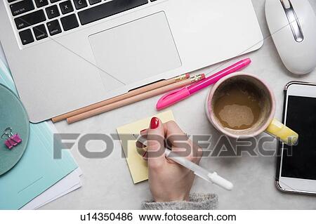 Stock Photograph - Woman writing on notepad at desk. Fotosearch