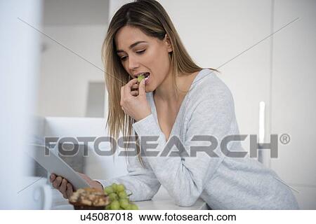Young woman eating white grapes and using digital tablet View Large Photo Image Stock Photo - Young woman eating white grapes and using digital tablet. Fotosearch
