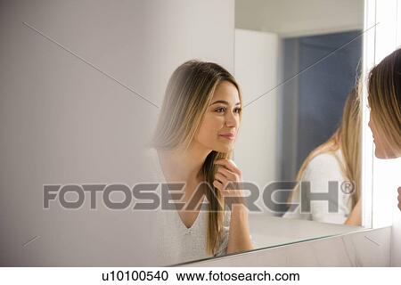 Stock Image - Young woman looking in mirror. Fotosearch