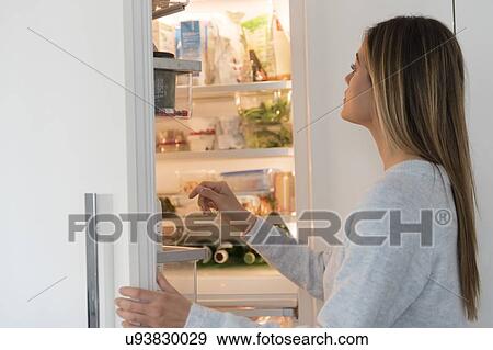 Stock Photo - Young woman looking into refrigerator. Fotosearch