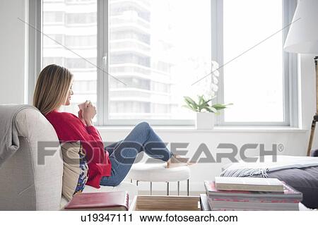 Stock Image - Young woman relaxing in living room. Fotosearch
