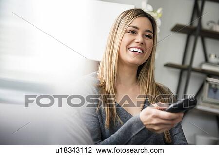 Stock Image - Young woman watching tv and laughing. Fotosearch