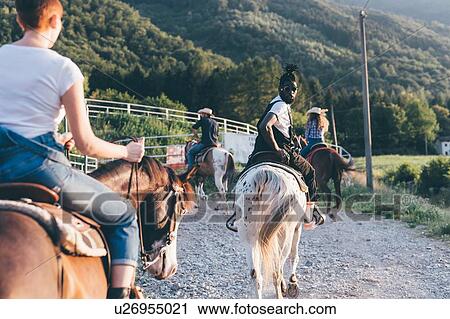 Stock Image - Adult friends riding horses on rural dirt track, rear view, Primaluna, Trentino-Alto Adige, Italy. Fotosearch