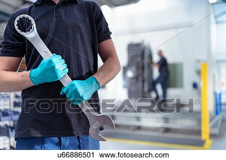 Stock Image - Ap0entice engineer holding large spanner in gearbox factory. Fotosearch