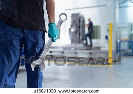 Stock Photo - Ap0entice engineer holding large spanner in gearbox factory. Fotosearch