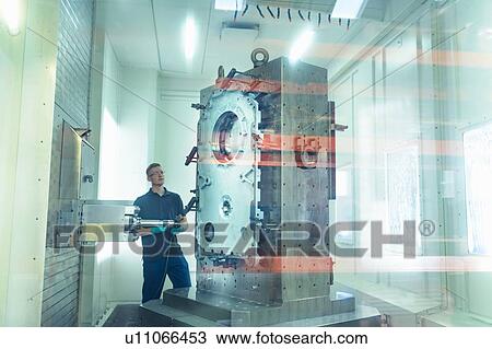 Stock Image - Ap0entice engineer setting up inside CNC machine in gearbox factory. Fotosearch