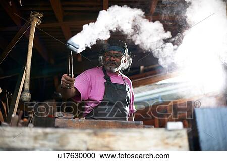 Stock Image - Blacksmith working in his forge. Fotosearch