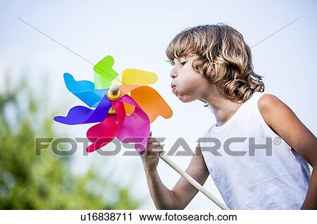 Stock Image - Boy blowing colourful paper windmill in park.. Fotosearch