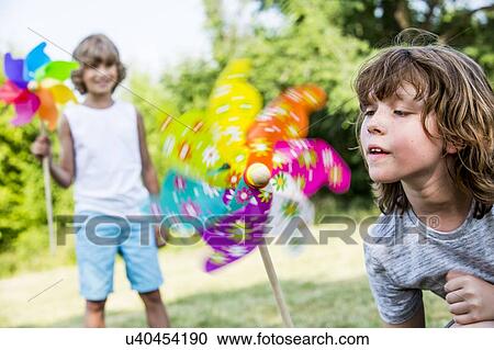 Stock Image - Boy blowing multi coloured paper windmill.. Fotosearch