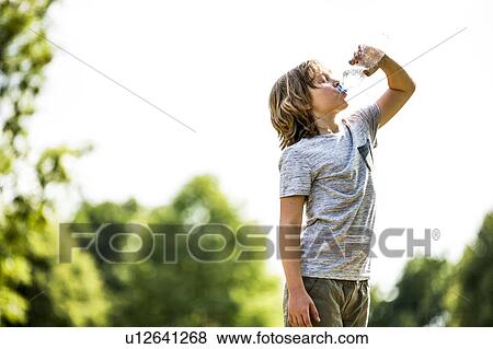 Stock Photo - Boy drinking water from plastic bottle in park.. Fotosearch