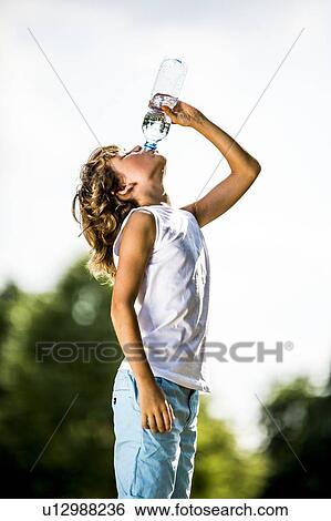 Stock Photograph - Boy drinking water from plastic bottle in park.. Fotosearch