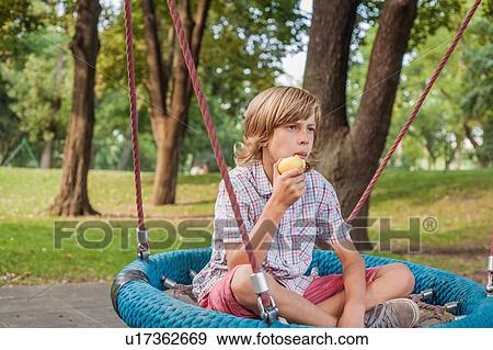 Boy eating fruit on web swing View Large Photo Image Stock Photo - Boy eating fruit on web swing. Fotosearch