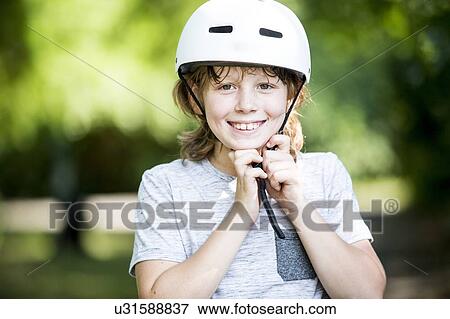 Stock Photo - Boy fastening bicycle helmet in park, smiling.. Fotosearch