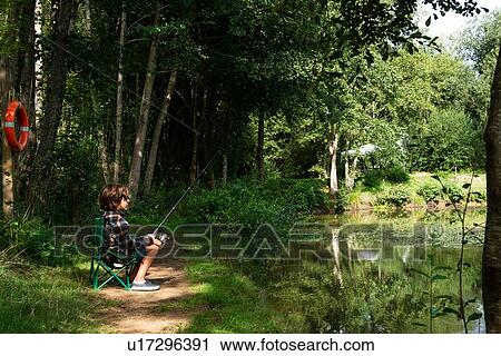 Stock Image - Boy fishing by lakeside, Bournemouth, UK. Fotosearch