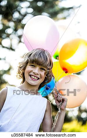 Picture - Boy holding bunch of balloons in park.. Fotosearch